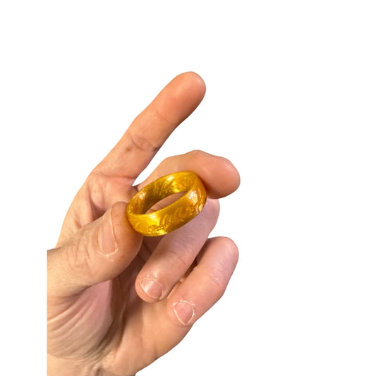 Gold-colored One Ring inspired costume prop held between fingers against a white background.