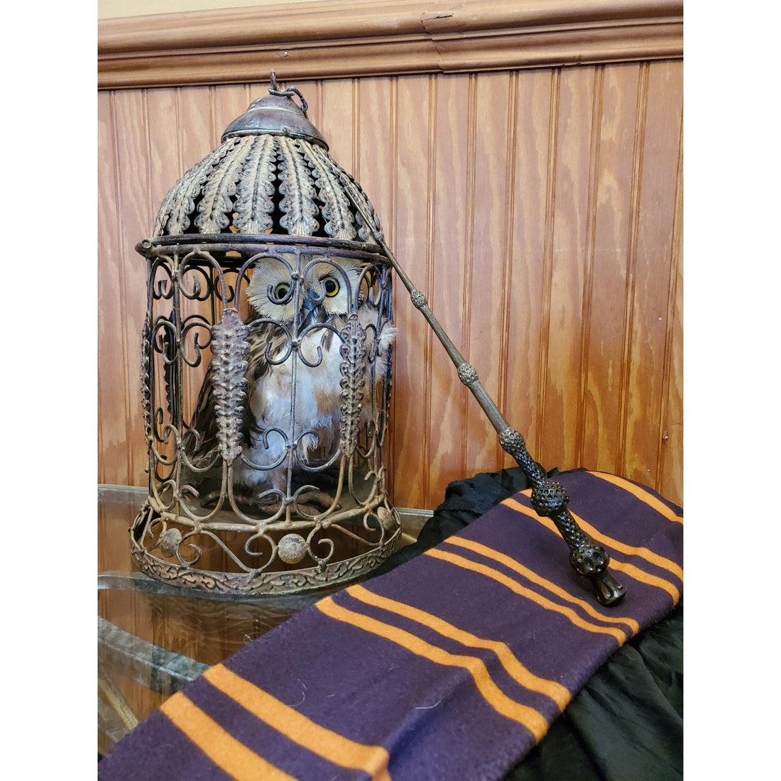 Textured Elder Wand inspired prop leaning beside an ornate cage with an owl figure and a striped scarf.